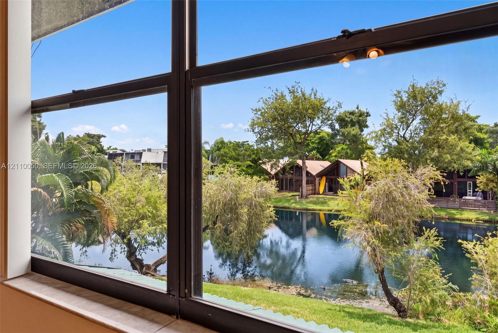 Large window featuring a metal frame and a stone-finish sill, showcasing exterior scenery including a pond, manicured landscaping, and mature trees