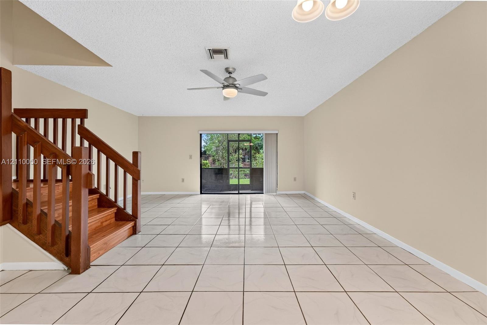 Open floor plan featuring large-format tile flooring, a wooden staircase with traditional railing, a brushed nickel ceiling fan, and sliding glass doors