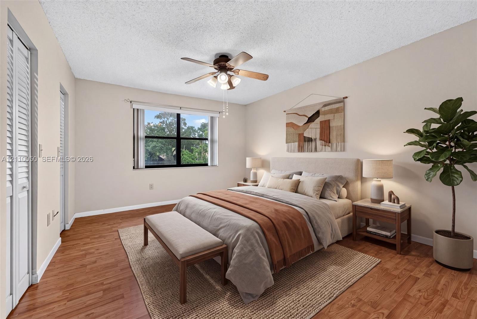 Wood-finish flooring, ceiling fan with integrated lighting, dual louvered-door closets, and a large multi-pane window