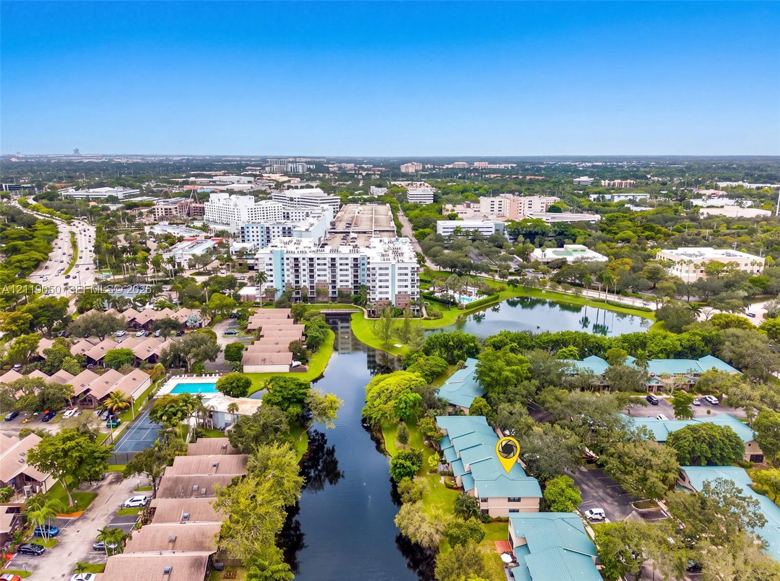 Aerial perspective featuring residential buildings positioned along a waterway with mature trees and proximity to local infrastructure