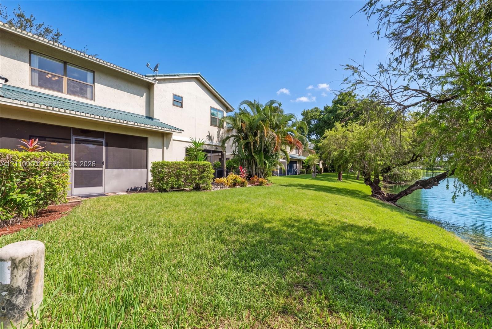 Exterior featuring a stucco facade, metal roof, screened-in porch, manicured lawn, and waterfront positioning