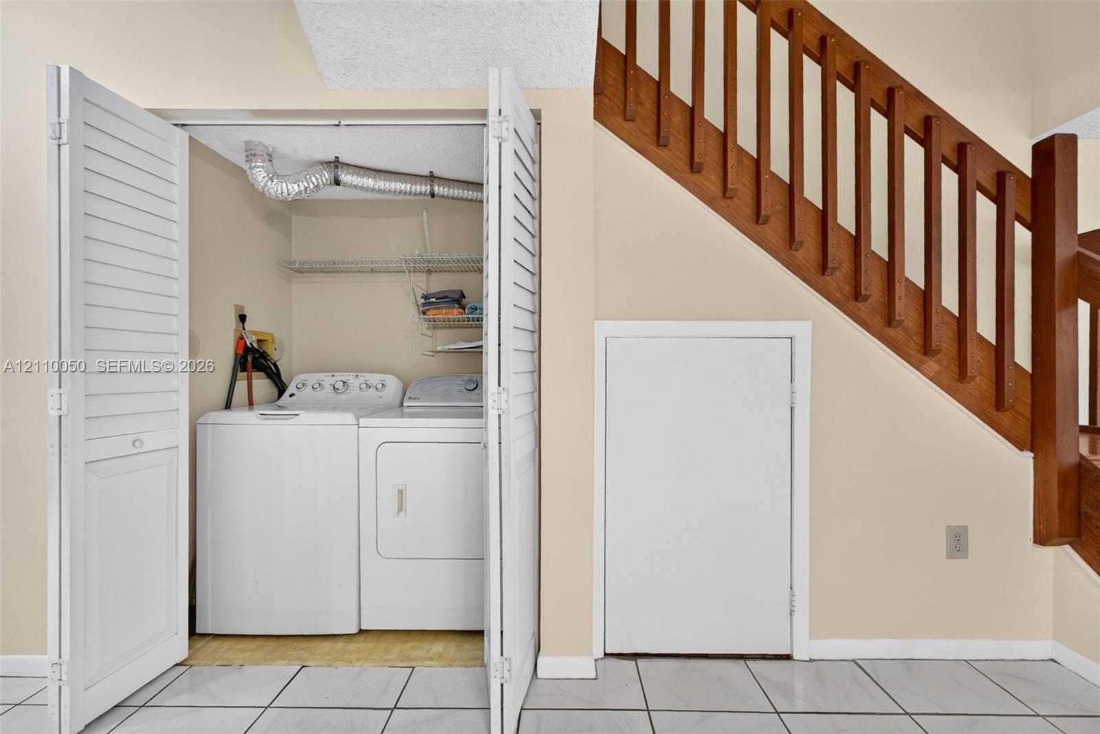 Laundry closet featuring louvered bifold doors and wire shelving, positioned beneath a wooden staircase with integrated railing