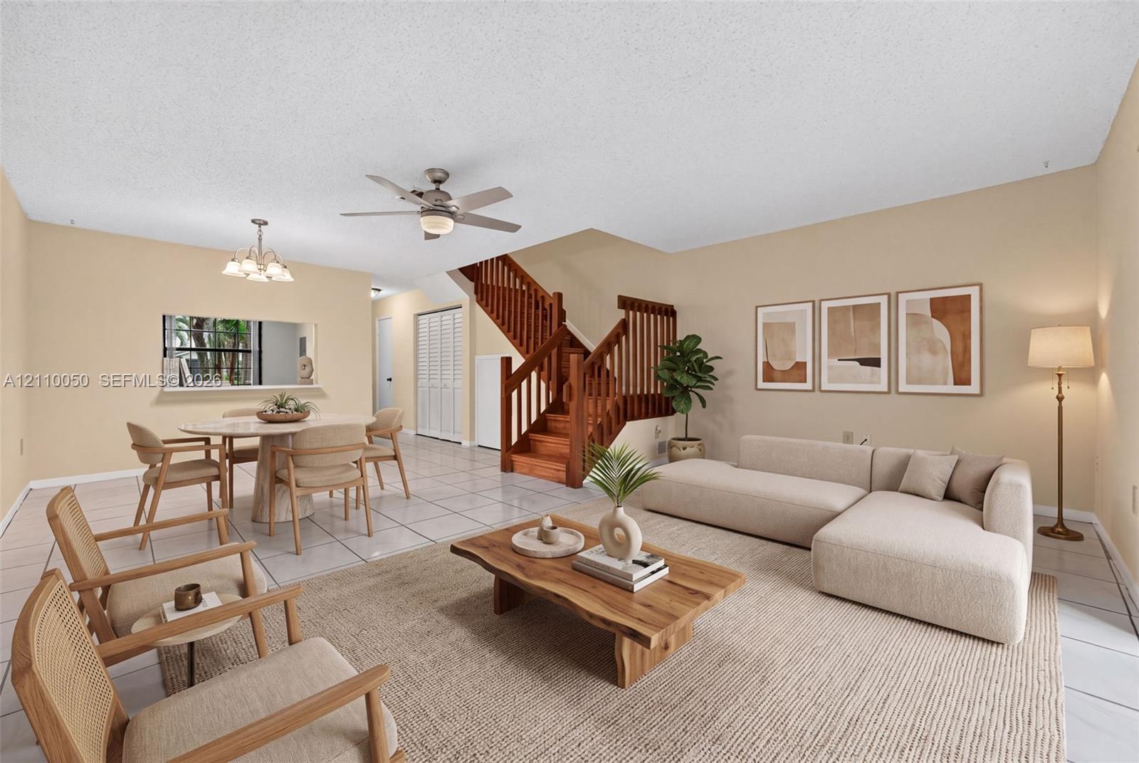 Open living area featuring large-format tile flooring, a staircase with wood railings and treads, a ceiling fan with integrated lighting, and a recessed window pass-through, virtually staged