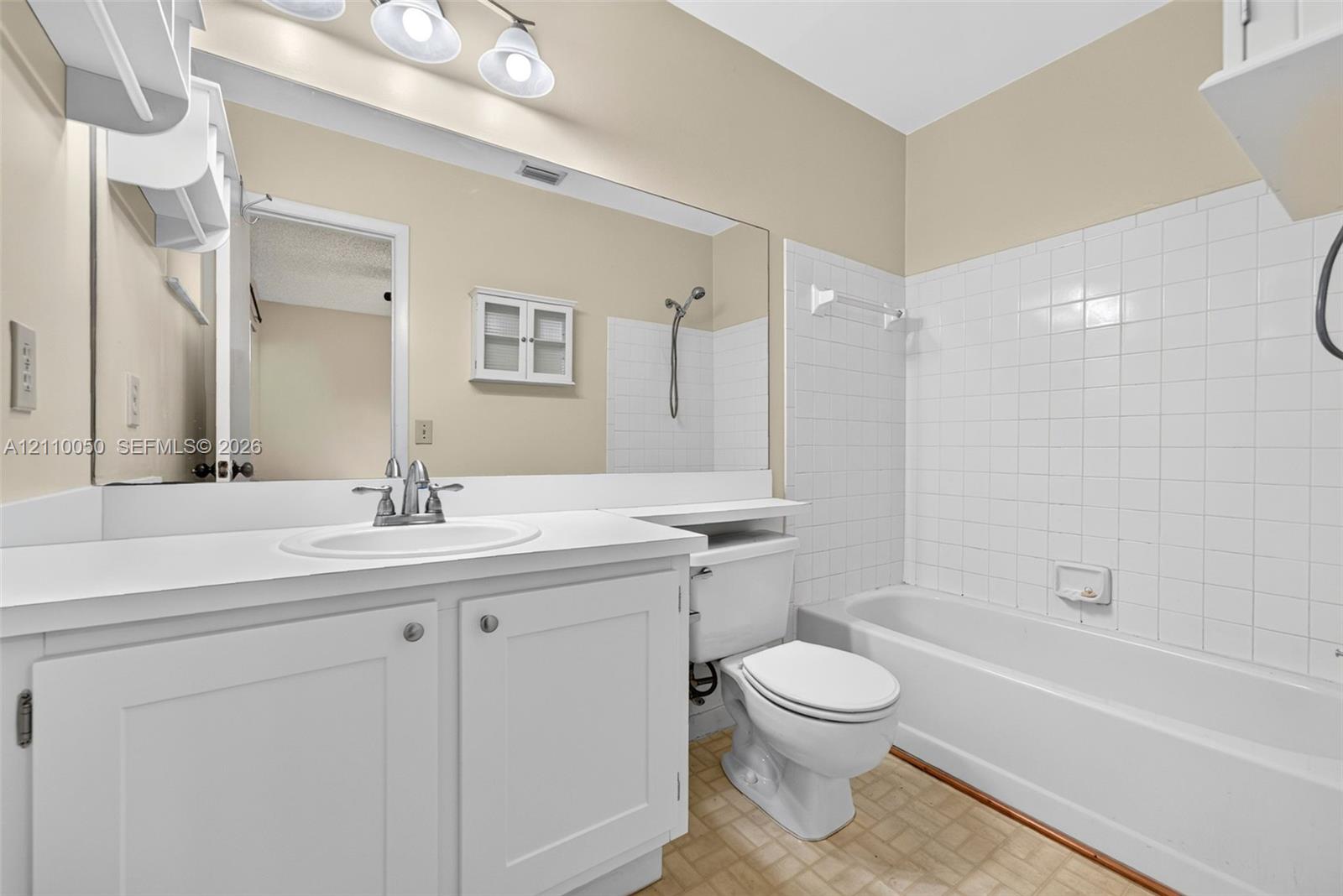 White cabinetry with an integrated countertop, large vanity mirror, three-light fixture, and tiled tub surround