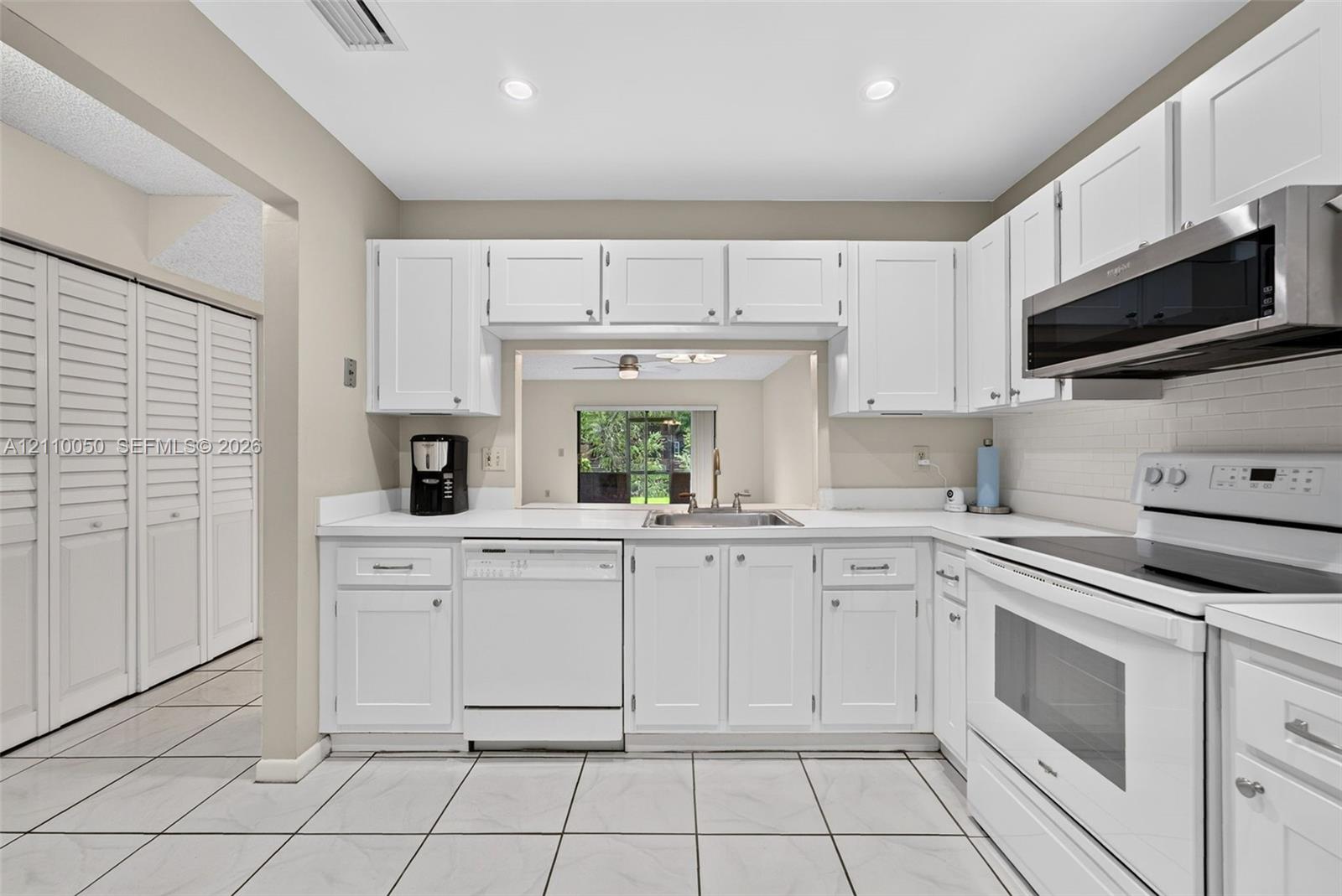 Kitchen featuring white shaker-style cabinetry, solid-surface countertops, recessed lighting, tile flooring, and a passthrough window