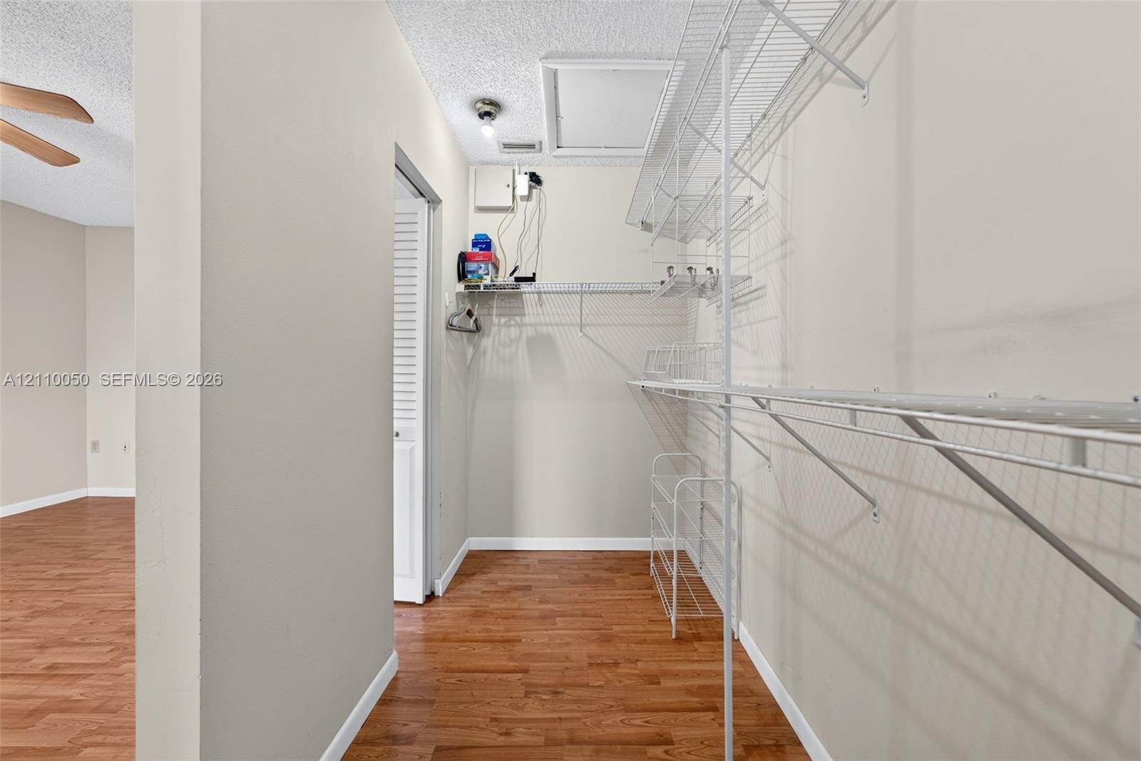 Storage area featuring wood-finish flooring, white wire shelving, and a ceiling access panel