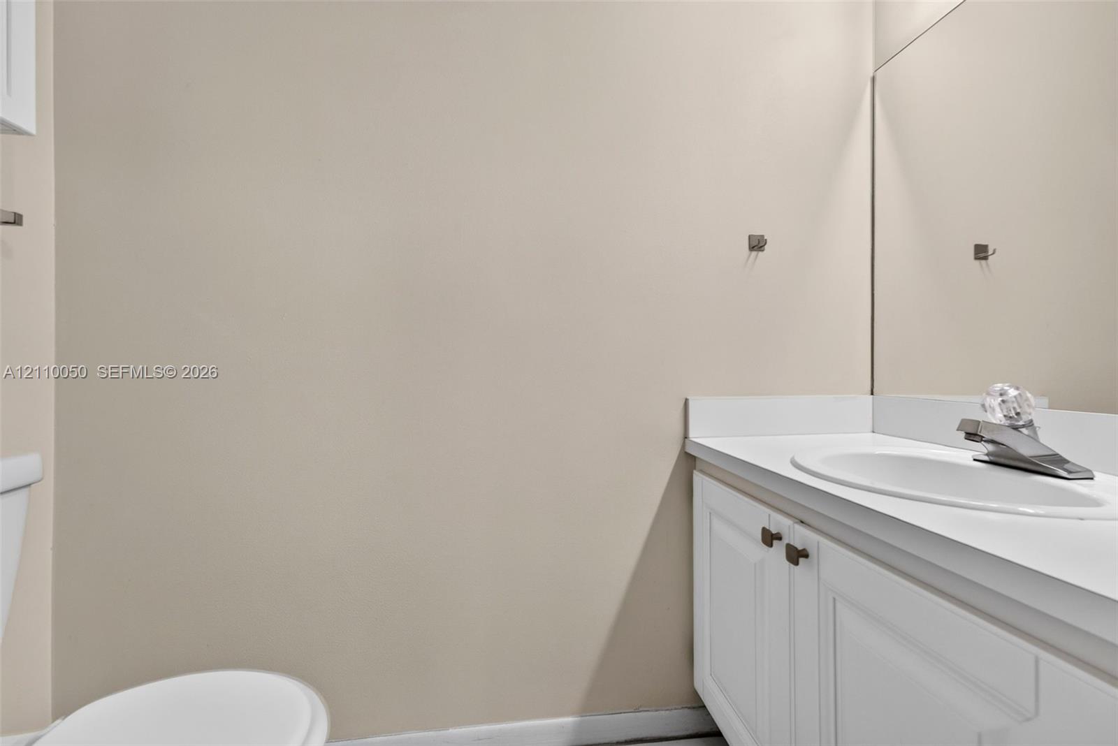 Vanity featuring a white cabinet base, solid surface countertop, integrated sink, and large wall-mounted mirror