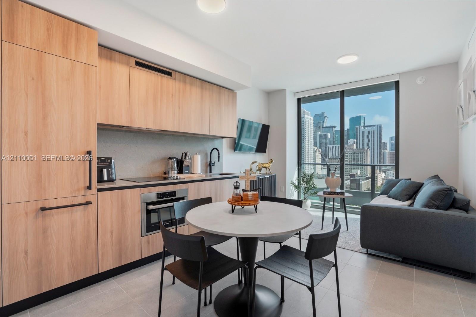 Kitchen featuring custom light-toned cabinetry, built-in panel-ready appliances, quartz countertops, and floor-to-ceiling glass sliding doors with an urban skyline backdrop