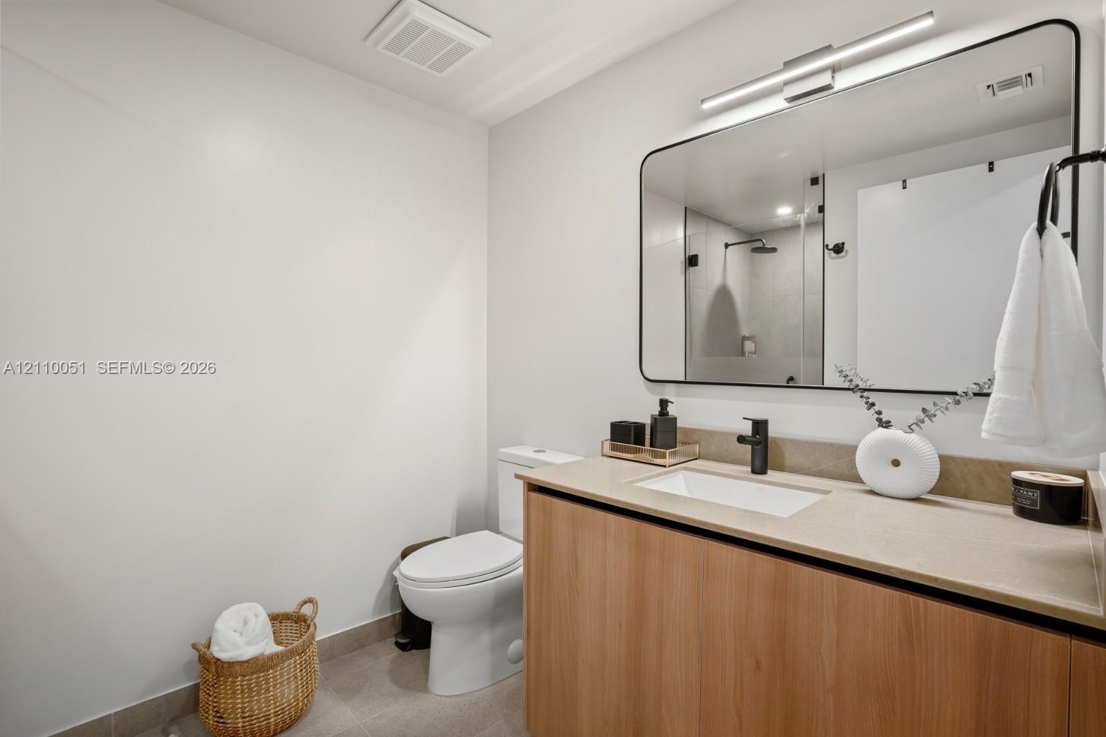 Wood-finish vanity cabinet with a stone-surface countertop, rectangular undermount sink, matte black faucet, and large rectangular mirror with rounded edges