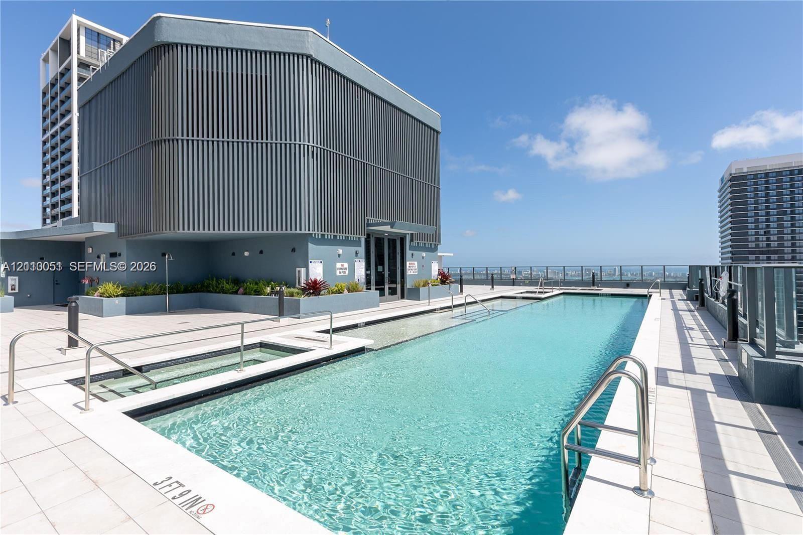 Rooftop swimming pool featuring a tiled deck, built-in hot tub, stainless steel ladders, and perimeter glass railing