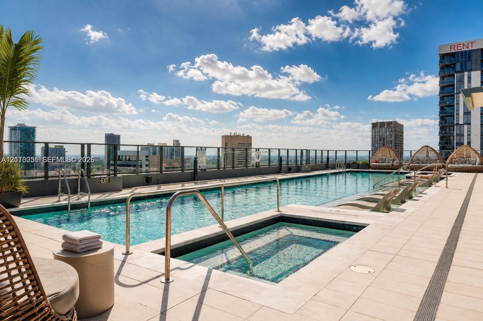 Rooftop swimming pool and spa featuring tiled decking, metal railing, and a city skyline backdrop
