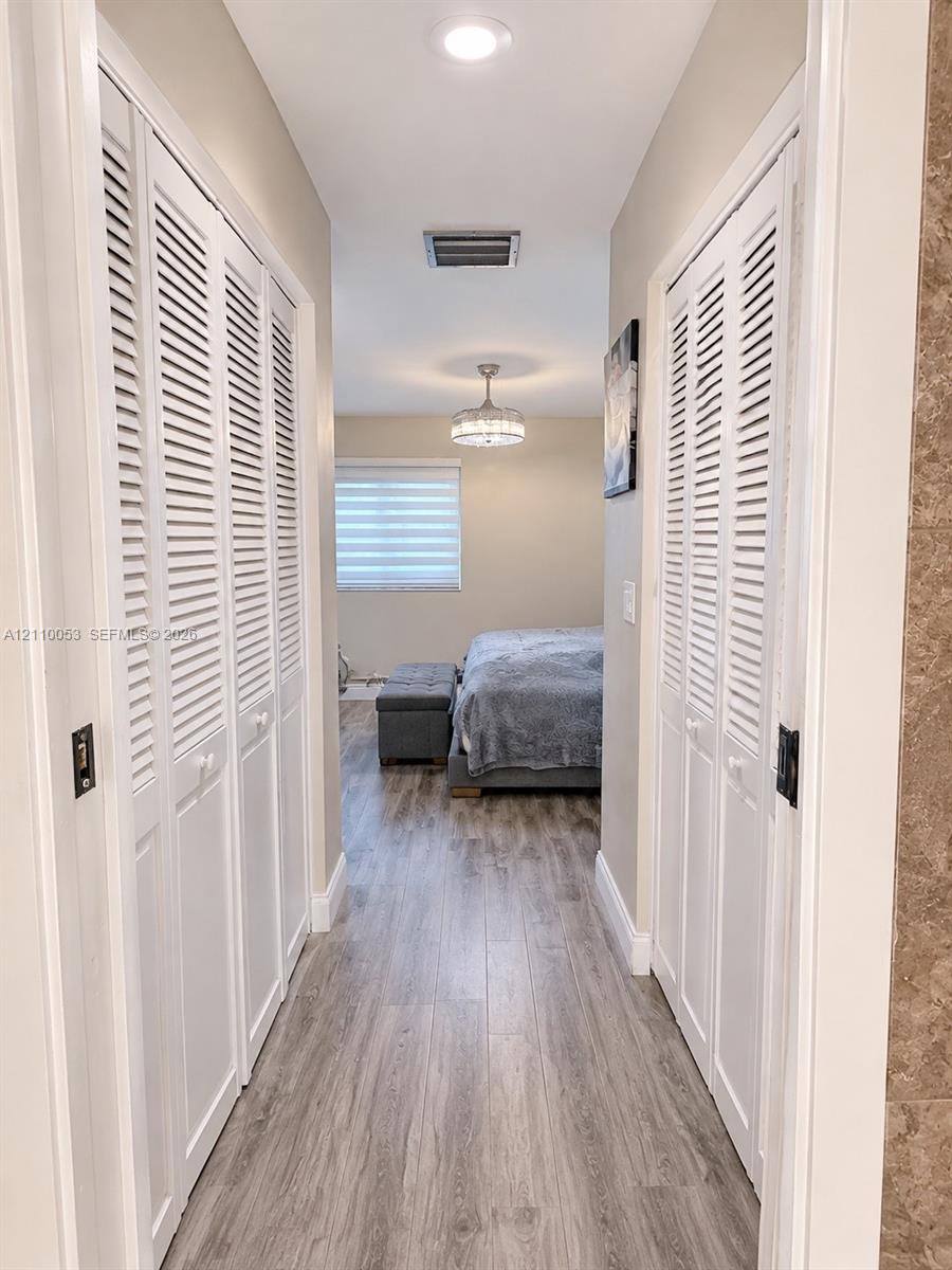 Hallway featuring wood-finish flooring, dual sets of white louvered-door closets, and recessed lighting
