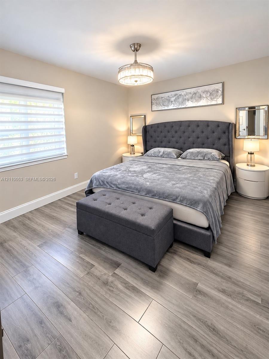 Wood-finish flooring, neutral wall tones, multi-tier drum ceiling fixture with crystal accents, and window with integrated blind system