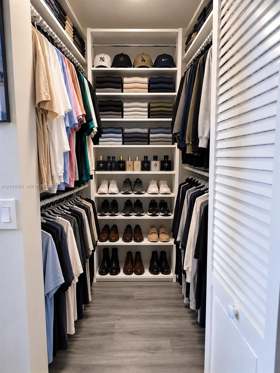 Walk-in closet featuring custom white built-in shelving, multi-level hanging rods, and wood-finish flooring