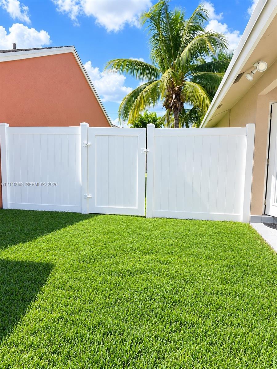Backyard featuring a white vinyl privacy fence with a gated entry and a manicured lawn