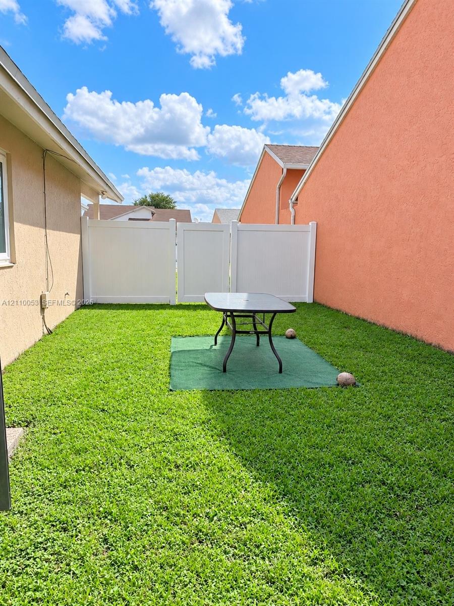 Side yard featuring a manicured lawn enclosed by a white vinyl privacy fence with a gated entry