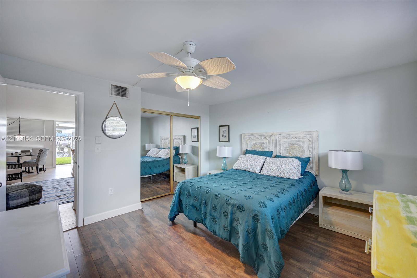 Bedroom featuring wood-finish flooring, a multi-blade ceiling fan with integrated lighting, and dual floor-to-ceiling mirrored closet doors