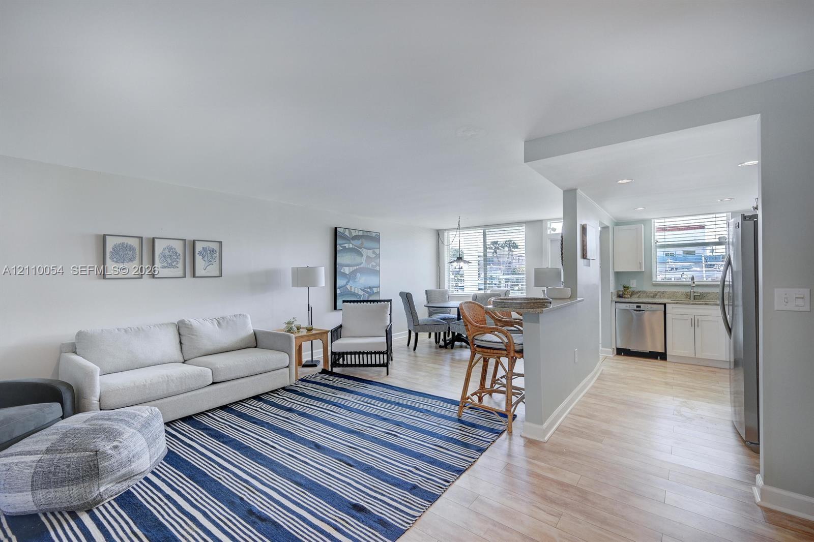 Open-concept interior featuring wood-finish flooring, a kitchen breakfast bar, recessed lighting, and white cabinetry