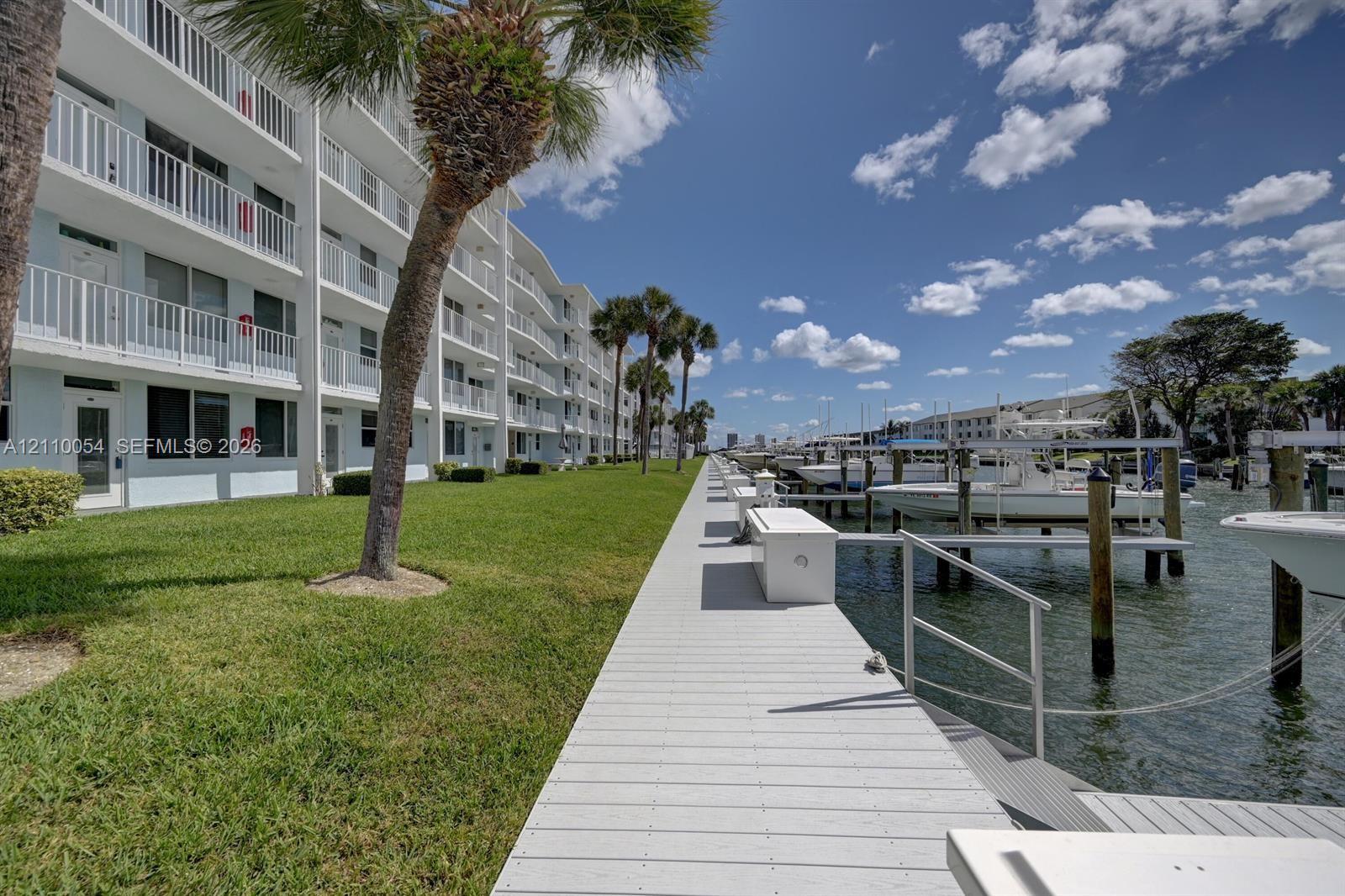 Waterfront property featuring a private boat dock, manicured green space, palm trees, and multi-level exterior balconies