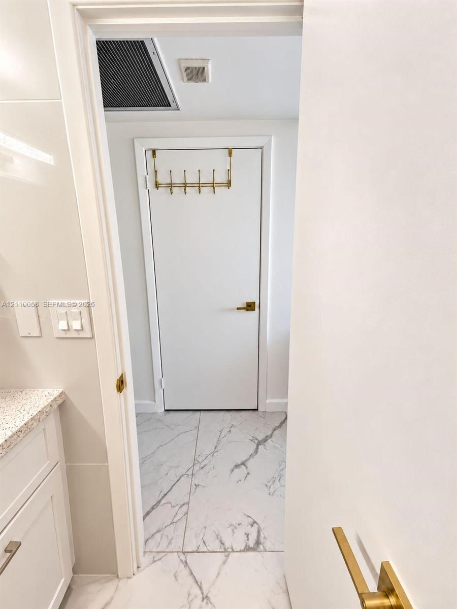 Stone-finish tile flooring, white cabinetry with stone-finish countertop, and brass-tone hardware