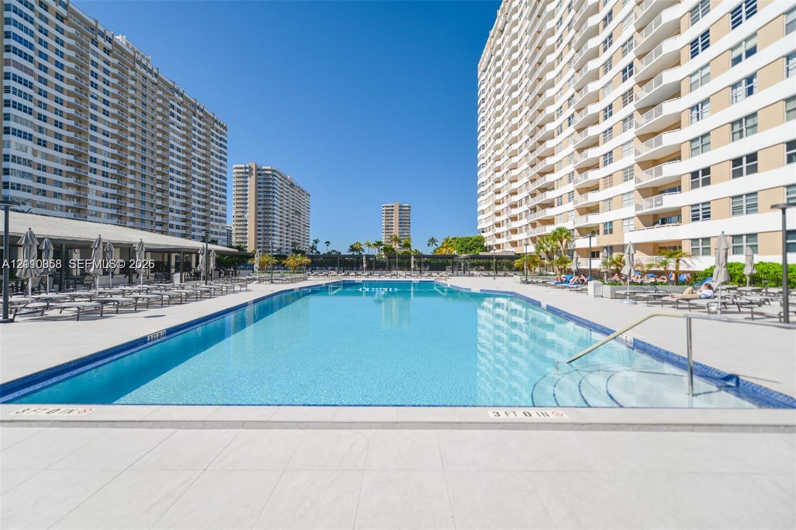 Large swimming pool with tiled perimeter, expansive paved deck area, metal handrails, and built-in steps