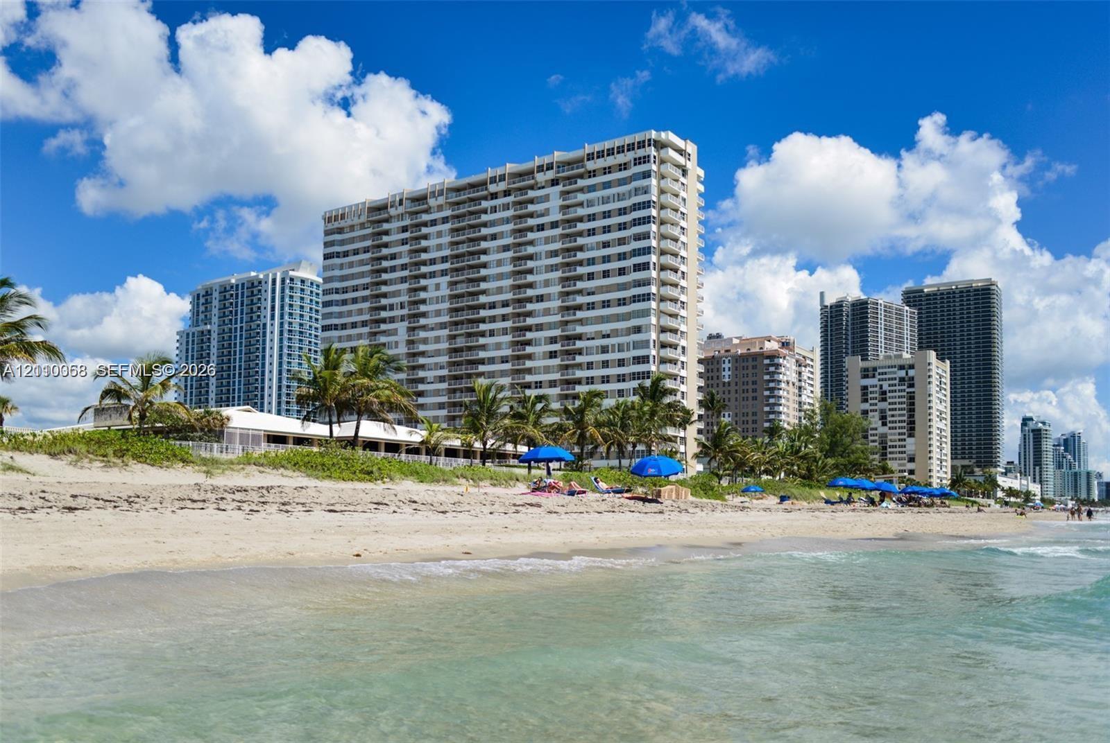 High-rise residential building featuring expansive glass-paneled balconies situated on a sand beach with direct shoreline access and native tropical landscaping