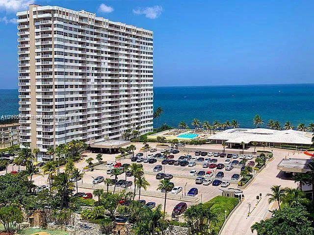 High-rise residential building featuring private balconies, surface parking, an outdoor swimming pool, and tropical landscaping