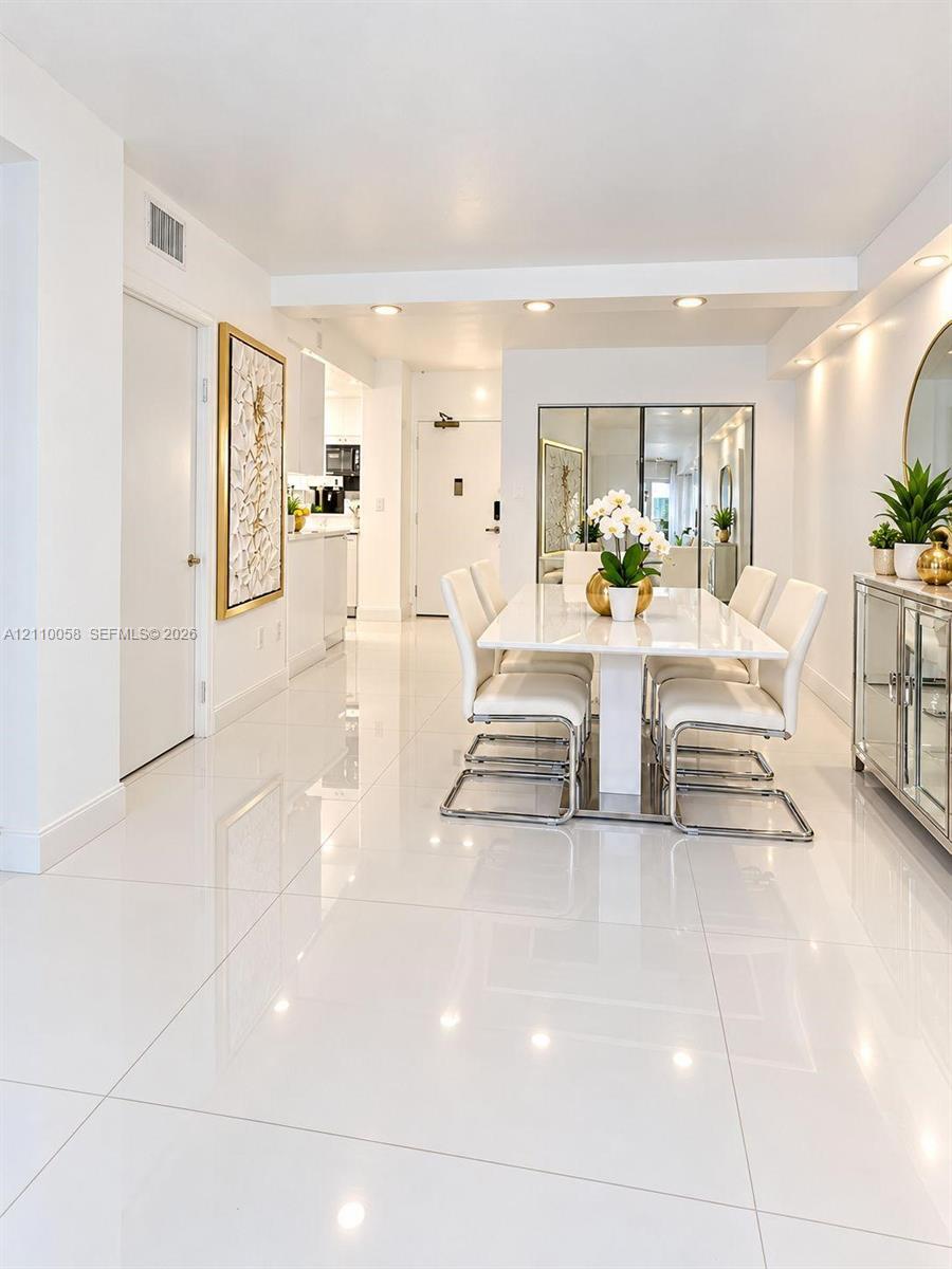Polished white tile flooring, recessed ceiling lighting, and mirrored wall accents