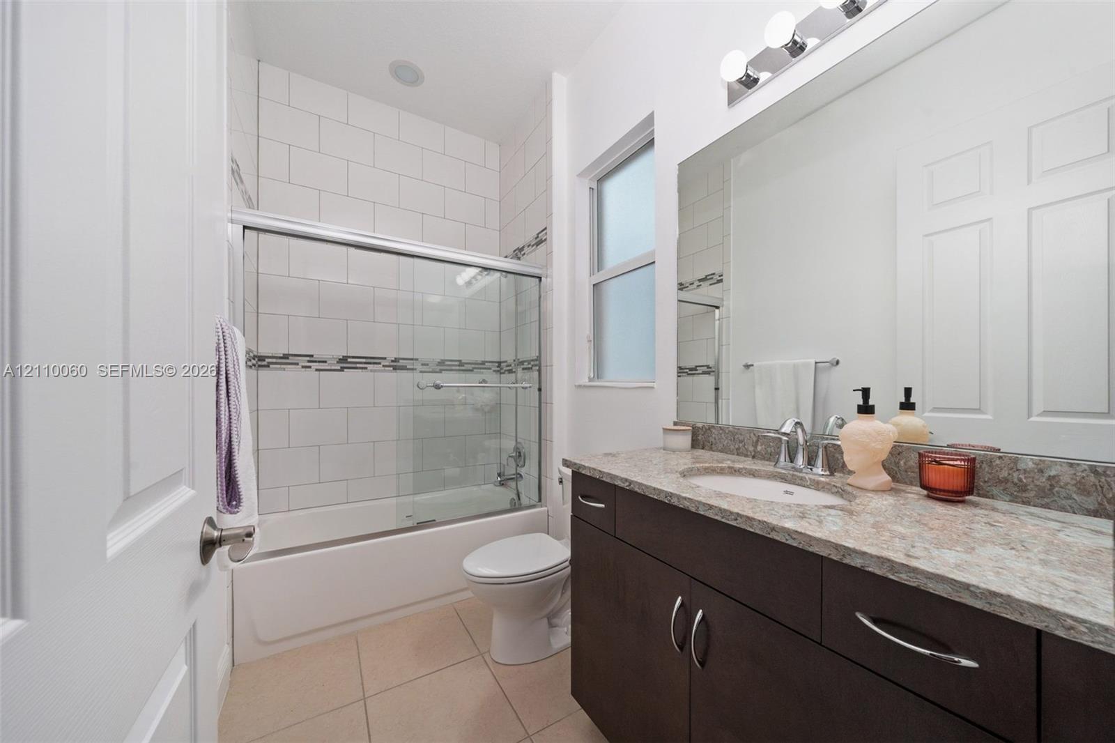 Bathroom featuring dark wood-finish cabinetry, a stone-patterned countertop, an integrated sink, a full-width vanity mirror, and a tub-shower combination with floor-to-ceiling subway tile