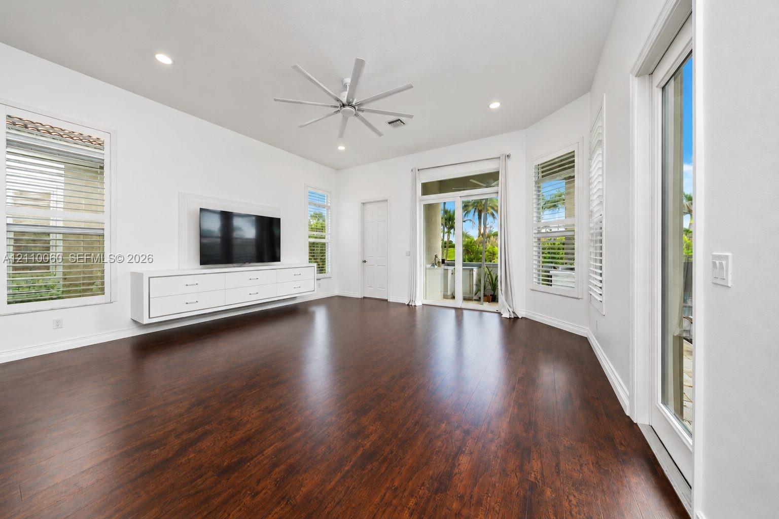 Interior space featuring dark wood-finish flooring, recessed lighting, a modern multi-blade ceiling fan, and a wall-mounted floating media console