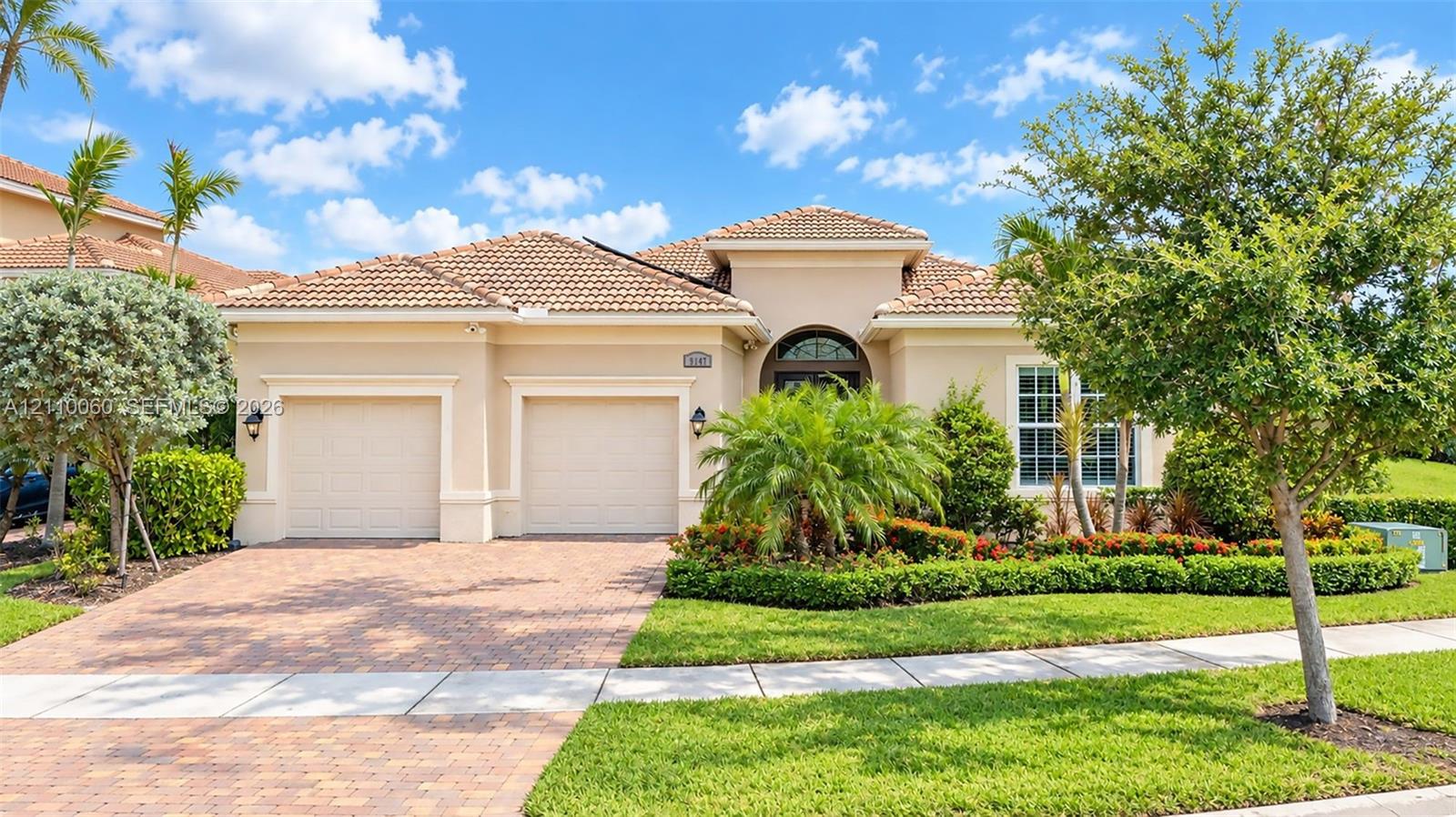 Stucco exterior featuring a multi-hipped tile roof, a two-car garage, and a paver driveway, complemented by professional landscaping Stucco exterior featuring a multi-hipped tile roof, a two-car garage, and a paver driveway, complemented by professional landscaping