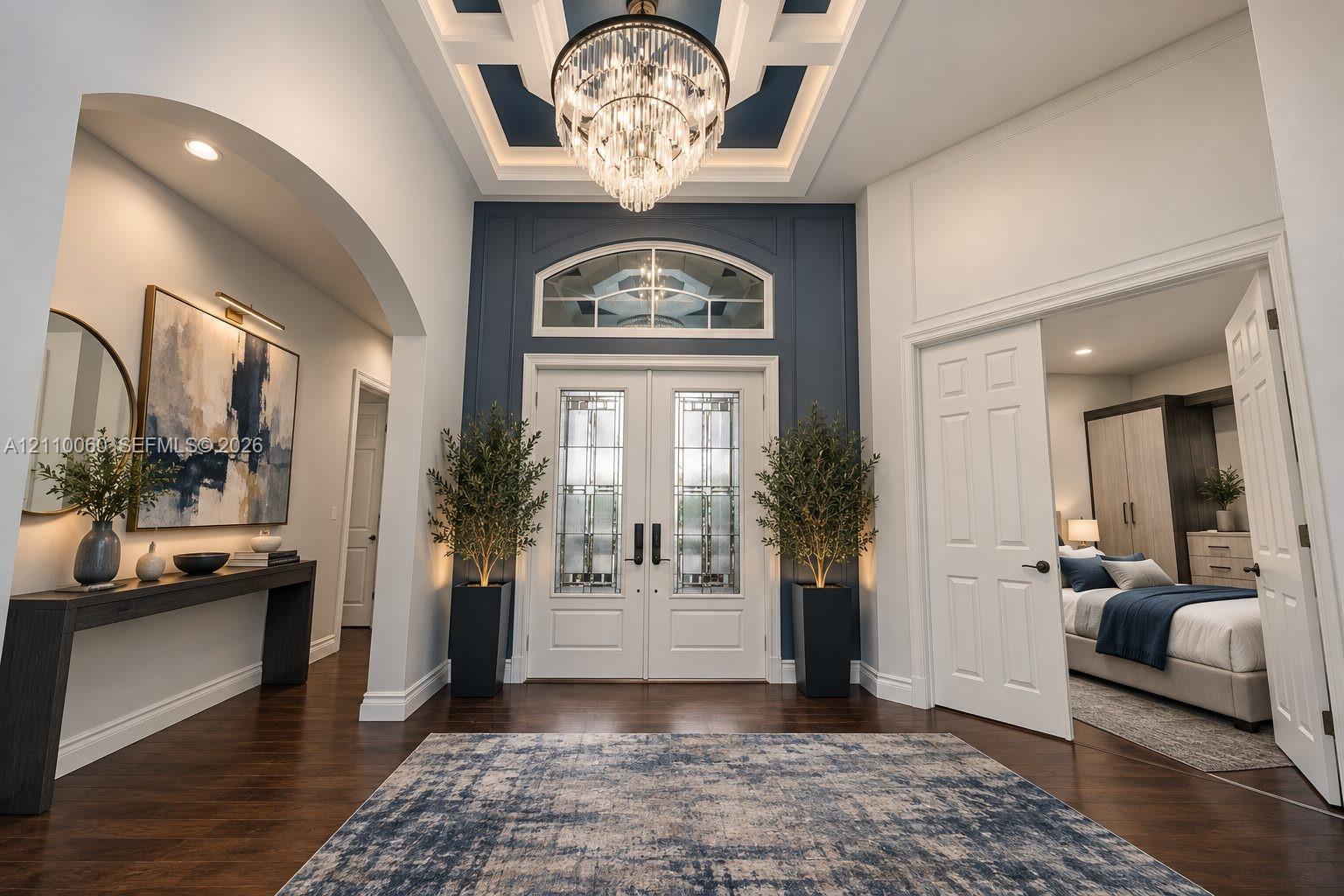 Virtually staged. Foyer featuring wood-finish flooring, a coffered ceiling with a crystal chandelier, arched entryway, and double entry doors with decorative glass inserts