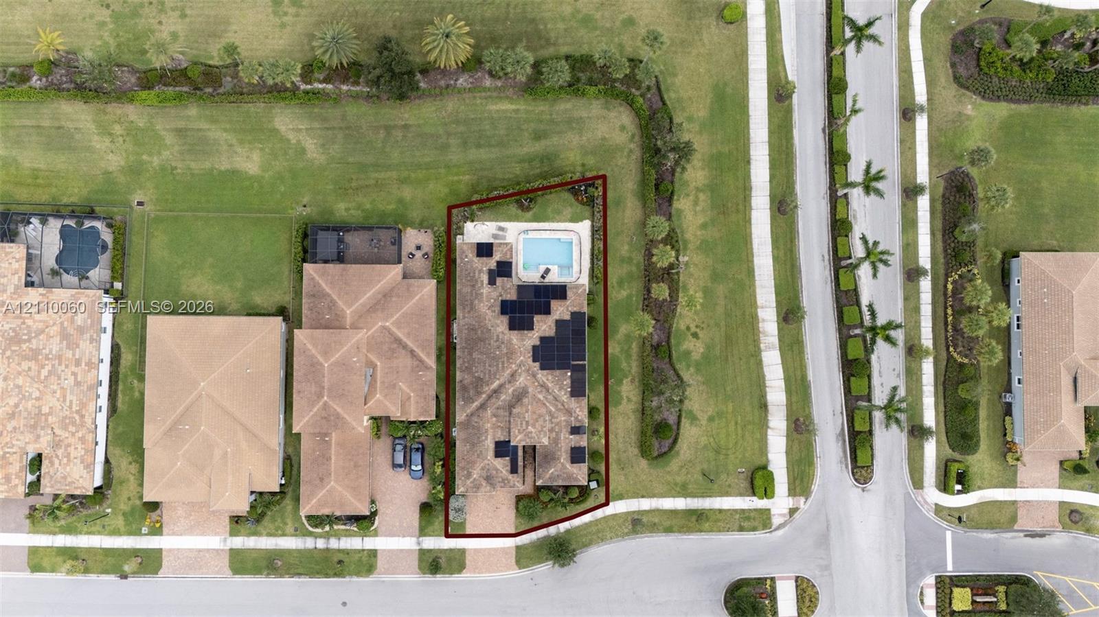 Aerial view of a corner lot property featuring a tiled roof, integrated rooftop solar panel system, private swimming pool, and paved driveway