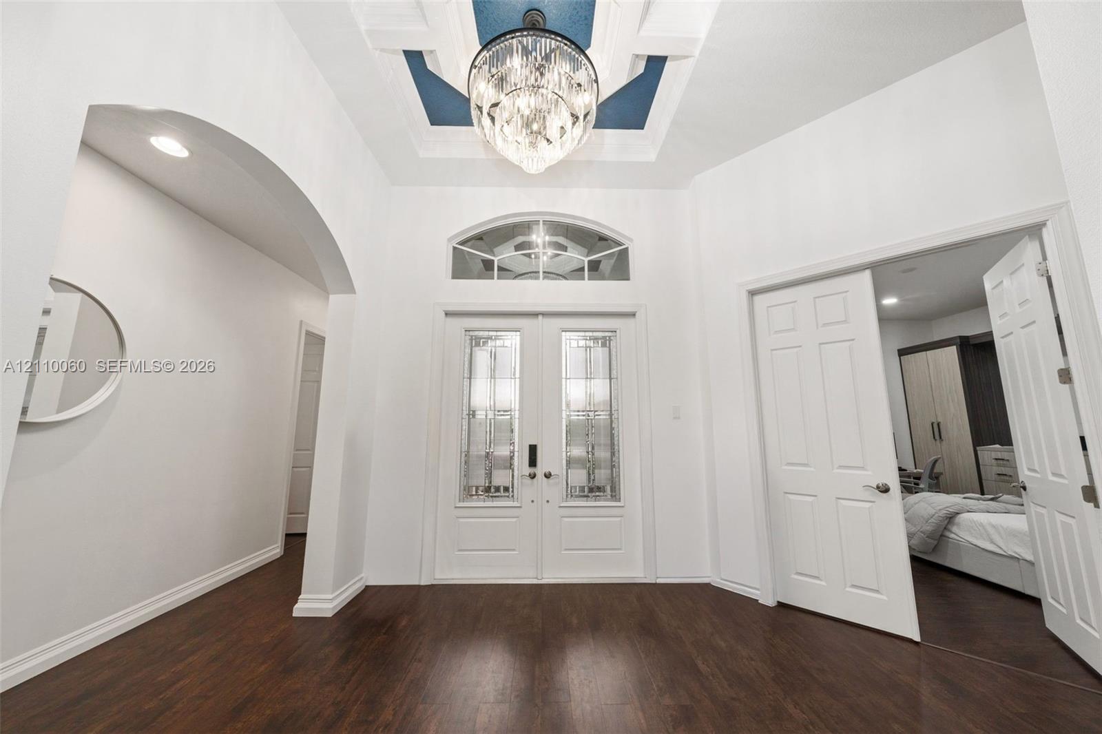 Foyer featuring double entry doors with decorative glass inserts, a recessed tray ceiling with accent color, a crystal chandelier, arched architectural detailing, and wood-finish flooring