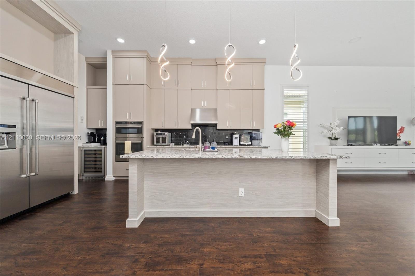 Kitchen featuring floor-to-ceiling cabinetry, a central island with stone countertop, stainless steel double wall ovens, built-in wine refrigeration, and decorative pendant lighting