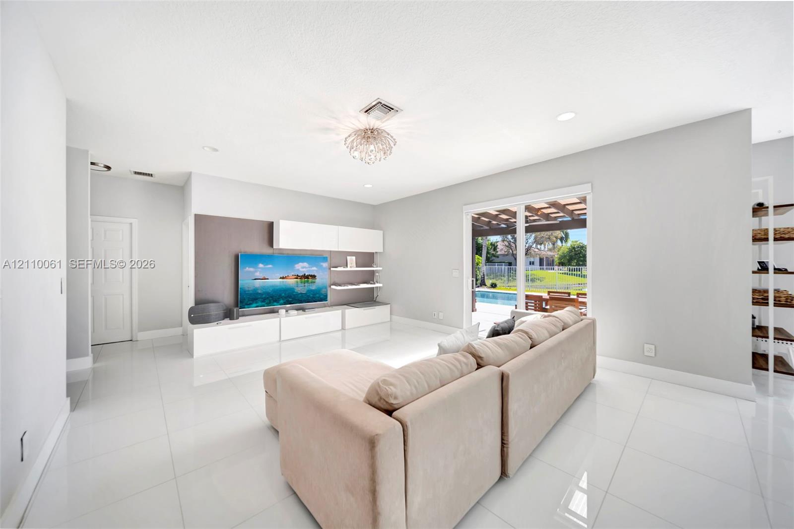 Open-concept living space featuring high-gloss tile flooring, recessed lighting, built-in media cabinetry with floating shelving, and sliding glass doors with access to a covered patio