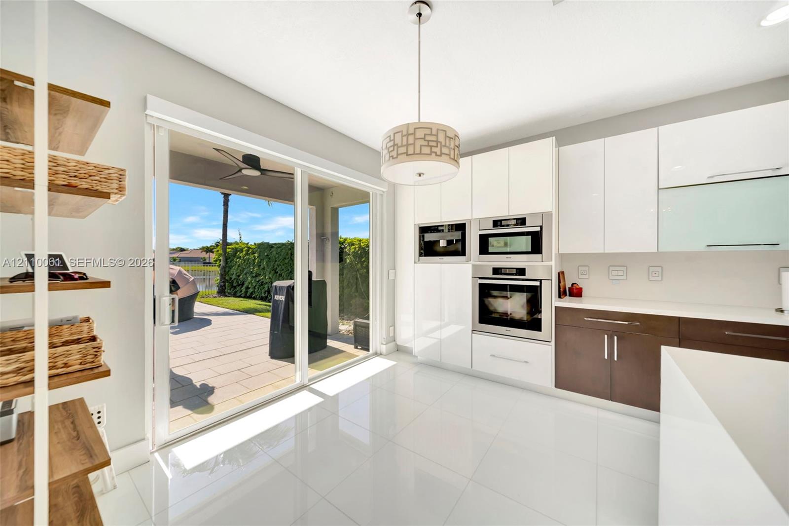 Kitchen featuring high-gloss white cabinetry, dual-tone lower storage, built-in stainless steel double wall ovens, large-format tile flooring, and sliding glass doors