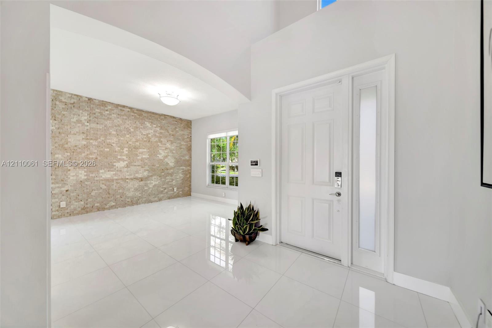 Foyer featuring high ceilings, large-format tile flooring, a prominent textured brick accent wall, and a solid-core entry door with a frosted glass sidelight