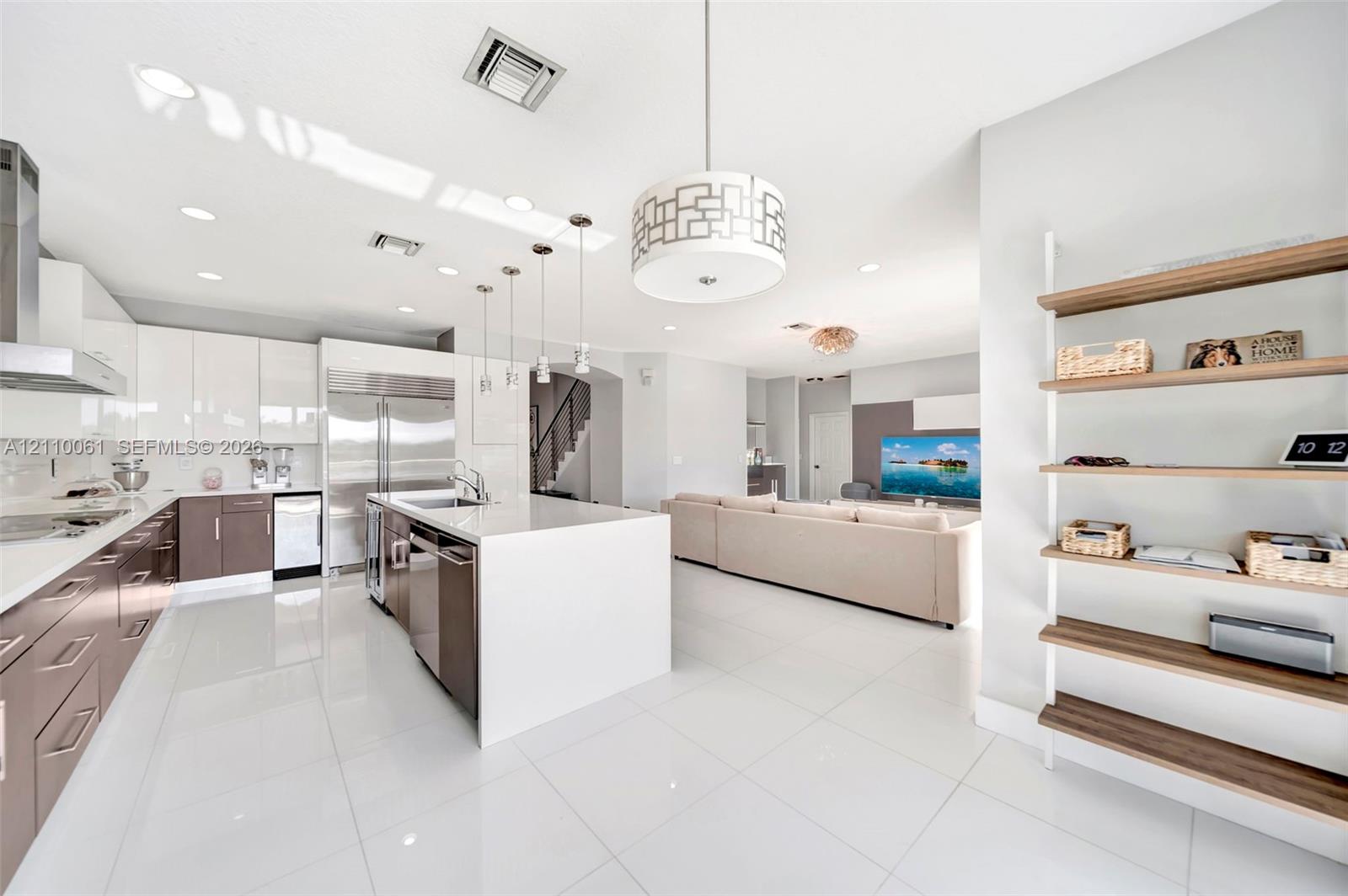 Modern kitchen featuring high-gloss cabinetry, a central island with quartz countertop, stainless steel appliances, polished tile flooring, and integrated pendant lighting