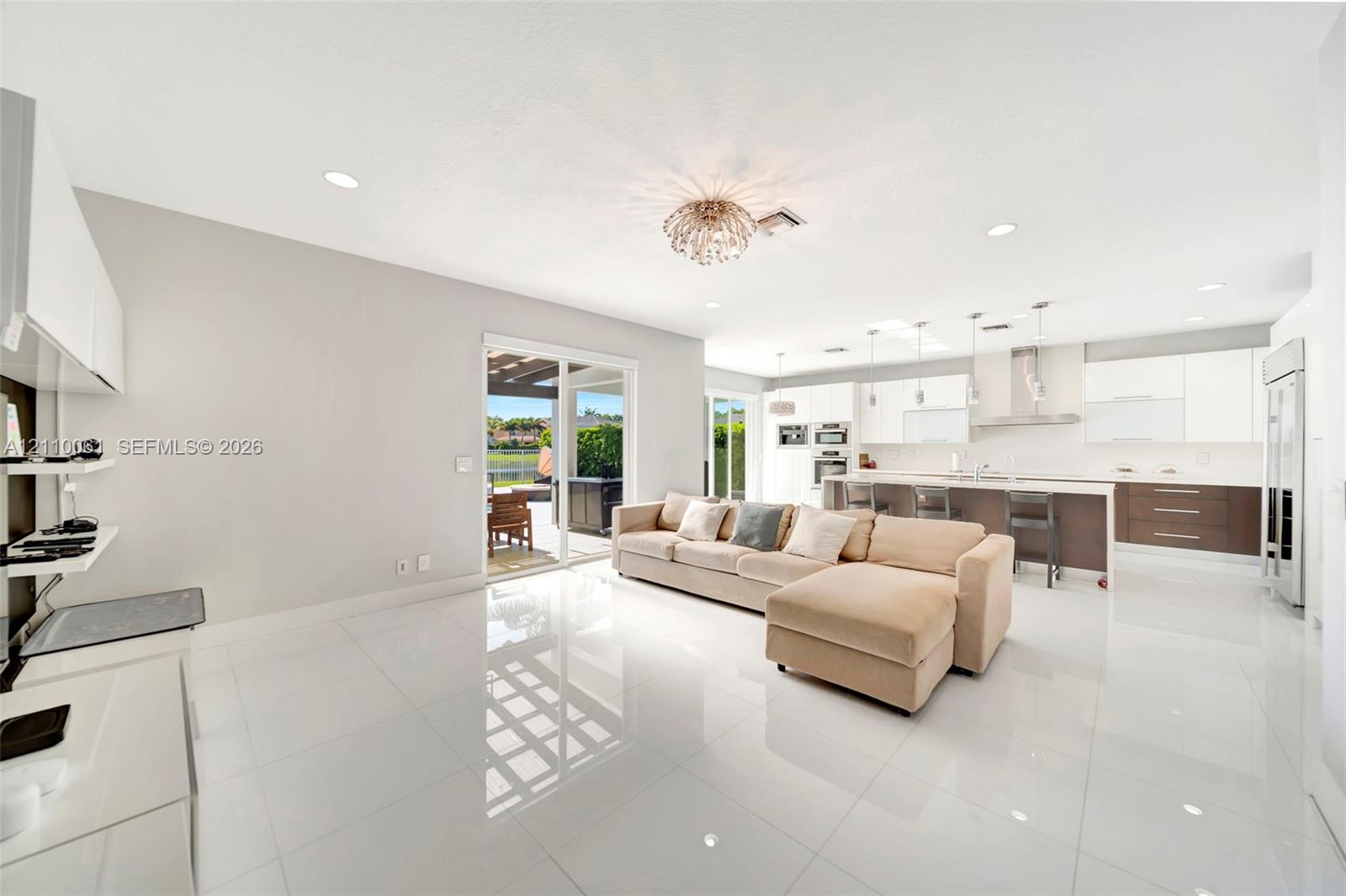 Open-concept living space featuring high-gloss tile flooring, recessed lighting, a modern chandelier, and a kitchen equipped with two-tone cabinetry and an expansive center island