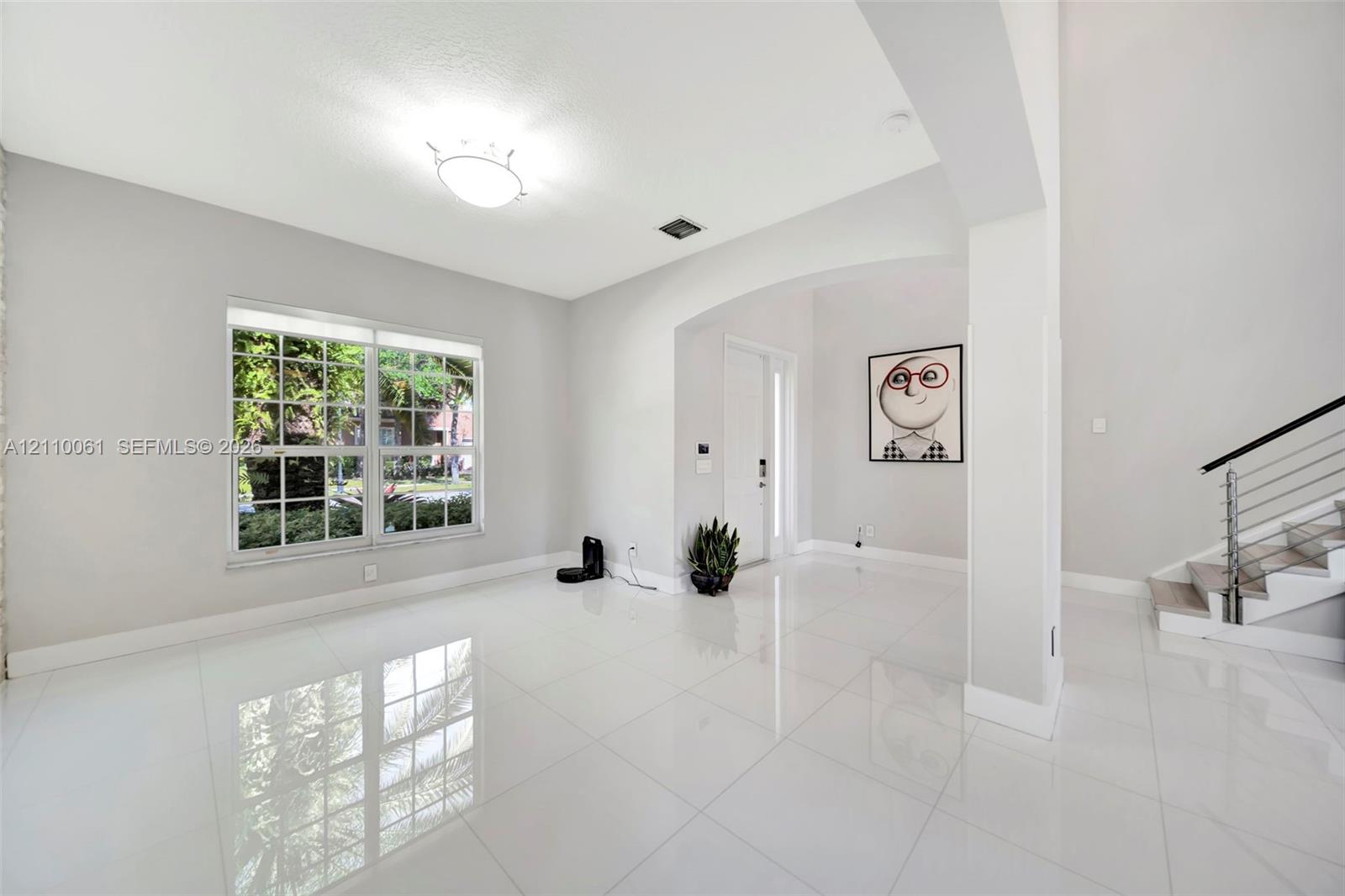 High-gloss tile flooring, arched architectural opening, multi-pane window, and staircase featuring a metal railing system