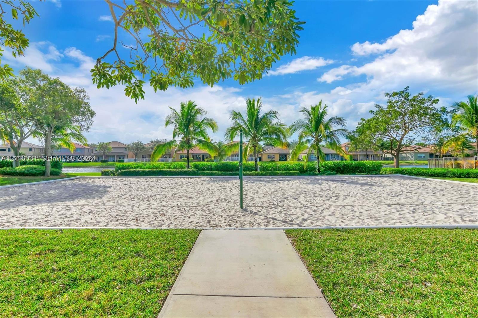 Sand volleyball court featuring a concrete walkway, perimeter landscaping, and mature palm trees