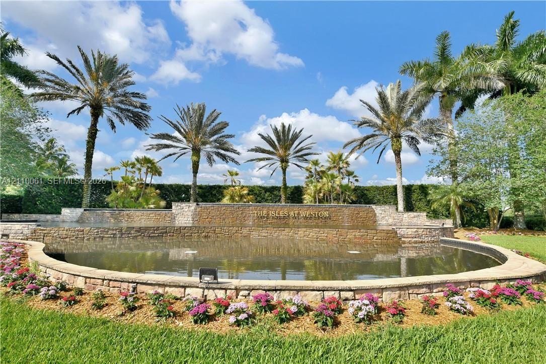 Stone-accented water feature, curated perimeter landscaping, mature palm trees, manicured turf, and tiered stone masonry walls