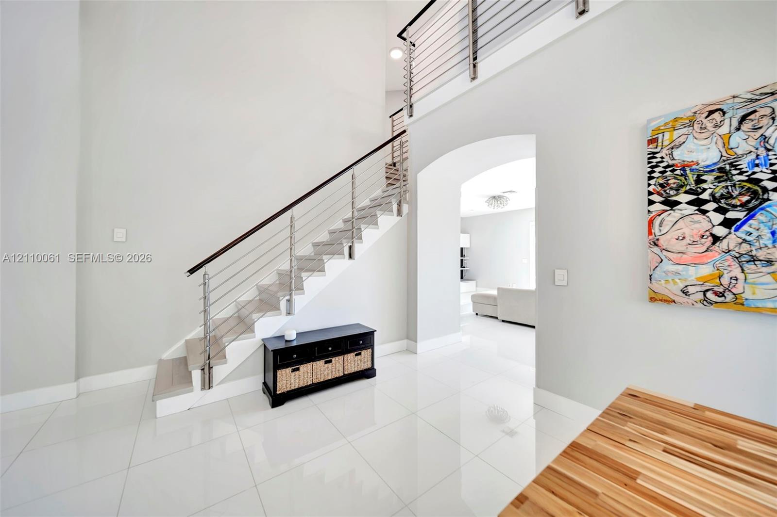 High-ceiling foyer featuring polished large-format tile flooring, a staircase with custom horizontal metal balusters, a dark wood handrail, and a recessed arched entry