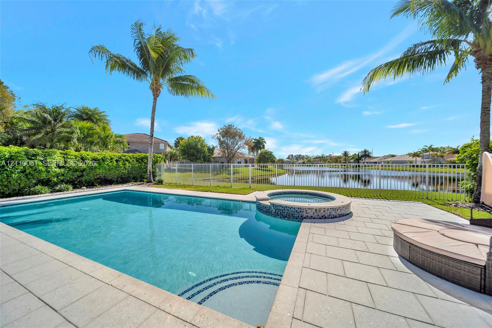 Swimming pool with integrated spillover spa, tiled deck, perimeter fencing, and mature palm trees