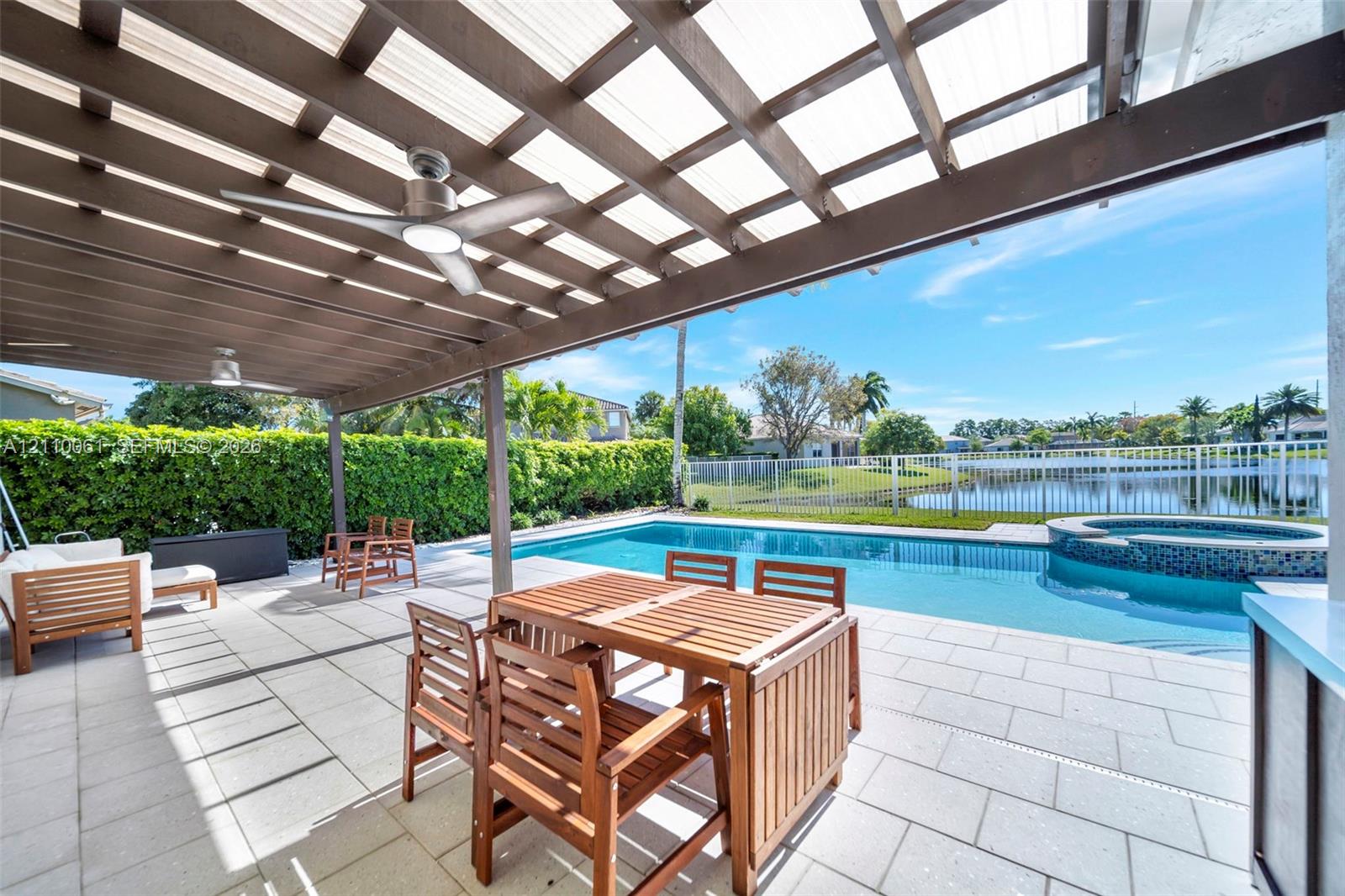 Covered patio featuring a wood-beam pergola, integrated ceiling fans, stone paver flooring, an in-ground pool, and a raised spillover spa