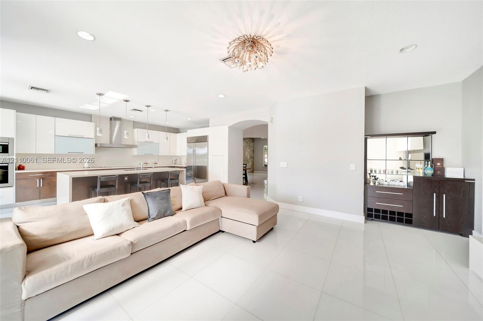 Open-concept space featuring polished tile flooring, two-tone cabinetry with an integrated breakfast bar, built-in stainless steel appliances, recessed ceiling lighting, and an ornamental metal light fixture