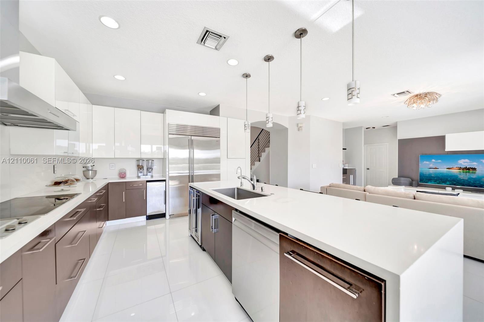 Kitchen featuring high-gloss white and dual-tone cabinetry, expansive solid-surface island, stainless steel appliances, and polished tile flooring