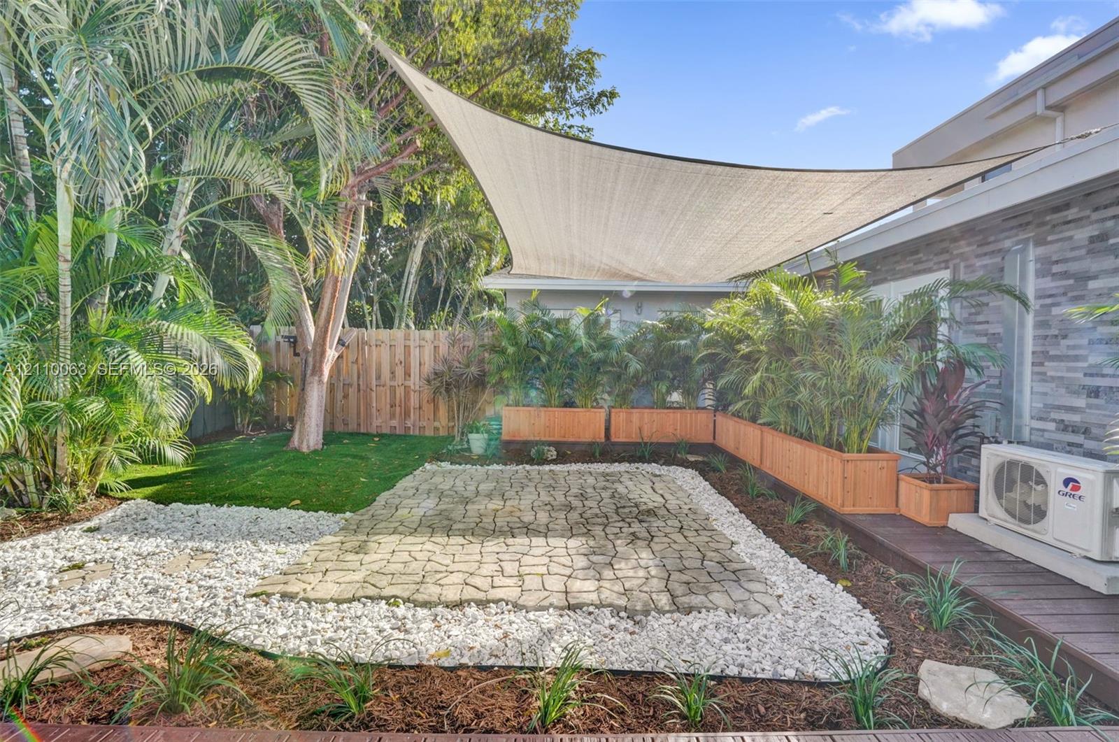 Private backyard featuring a paved stone patio, a custom overhead shade sail, integrated wood-finish planters, and a perimeter wood privacy fence