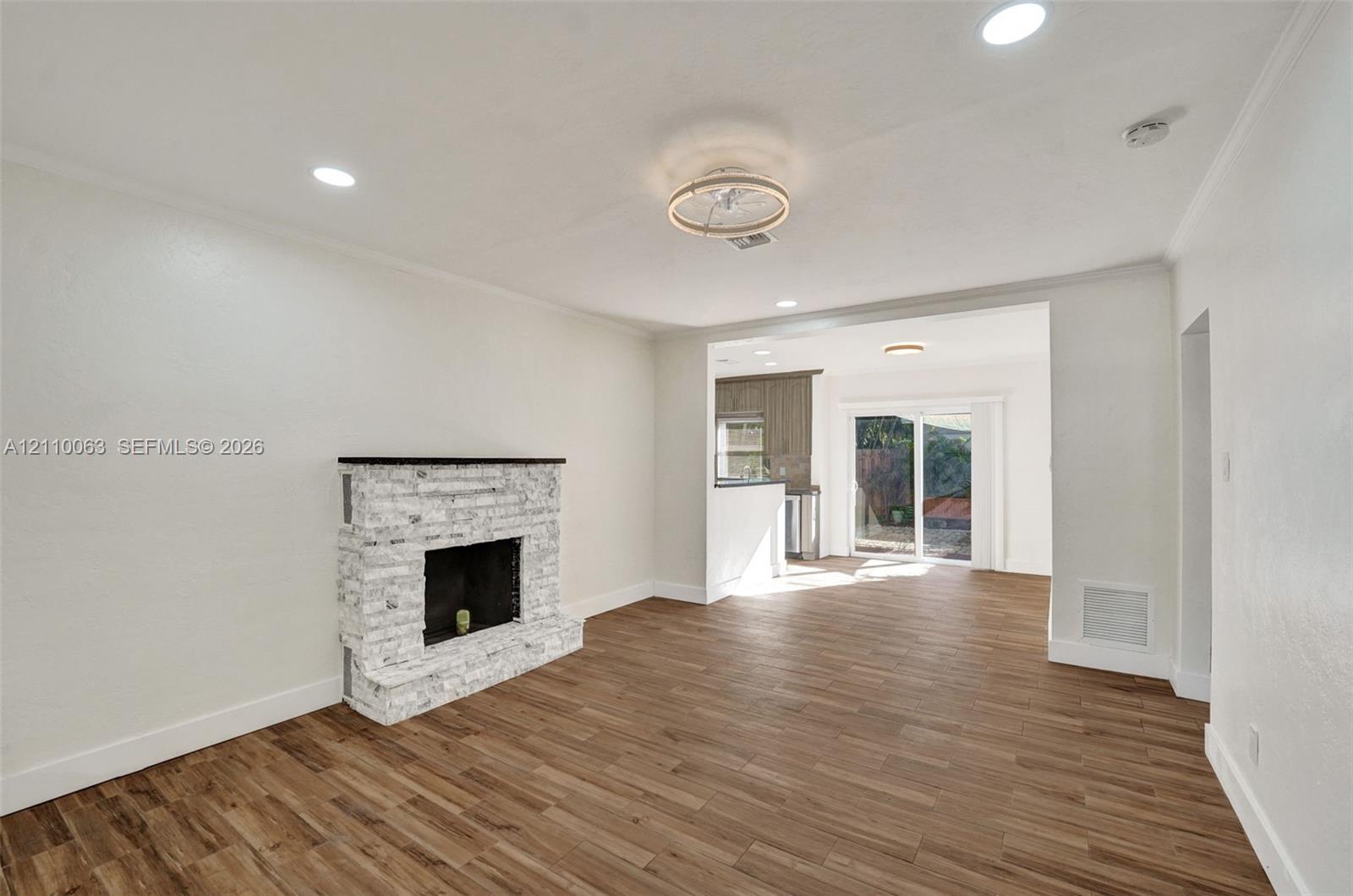 Wood-finish flooring, white stone-surround fireplace, recessed lighting, ceiling flush-mount fixture, and sliding glass door Wood-finish flooring, white stone-surround fireplace, recessed lighting, ceiling flush-mount fixture, and sliding glass door